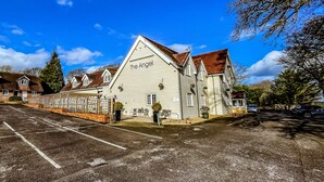 Un edificio blanco con el letrero "The Angel" en la fachada, un estacionamiento al frente y un cielo azul despejado.