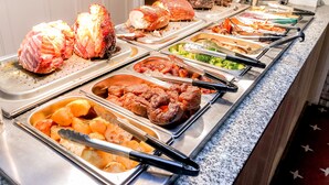 Un bufé con diversos platos, incluyendo carnes asadas, papas y vegetales.