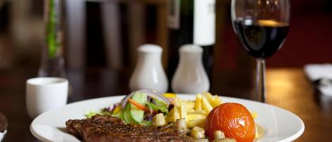 A plate with steak, fries, salad, and a tomato on a wooden table.