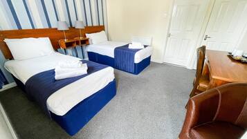 Habitación de hotel con dos camas, un cabecero de madera, una mesita con bandeja y una silla de cuero marrón.