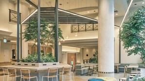 Um lobby moderno com área de estar central, várias mesas e uma escada.