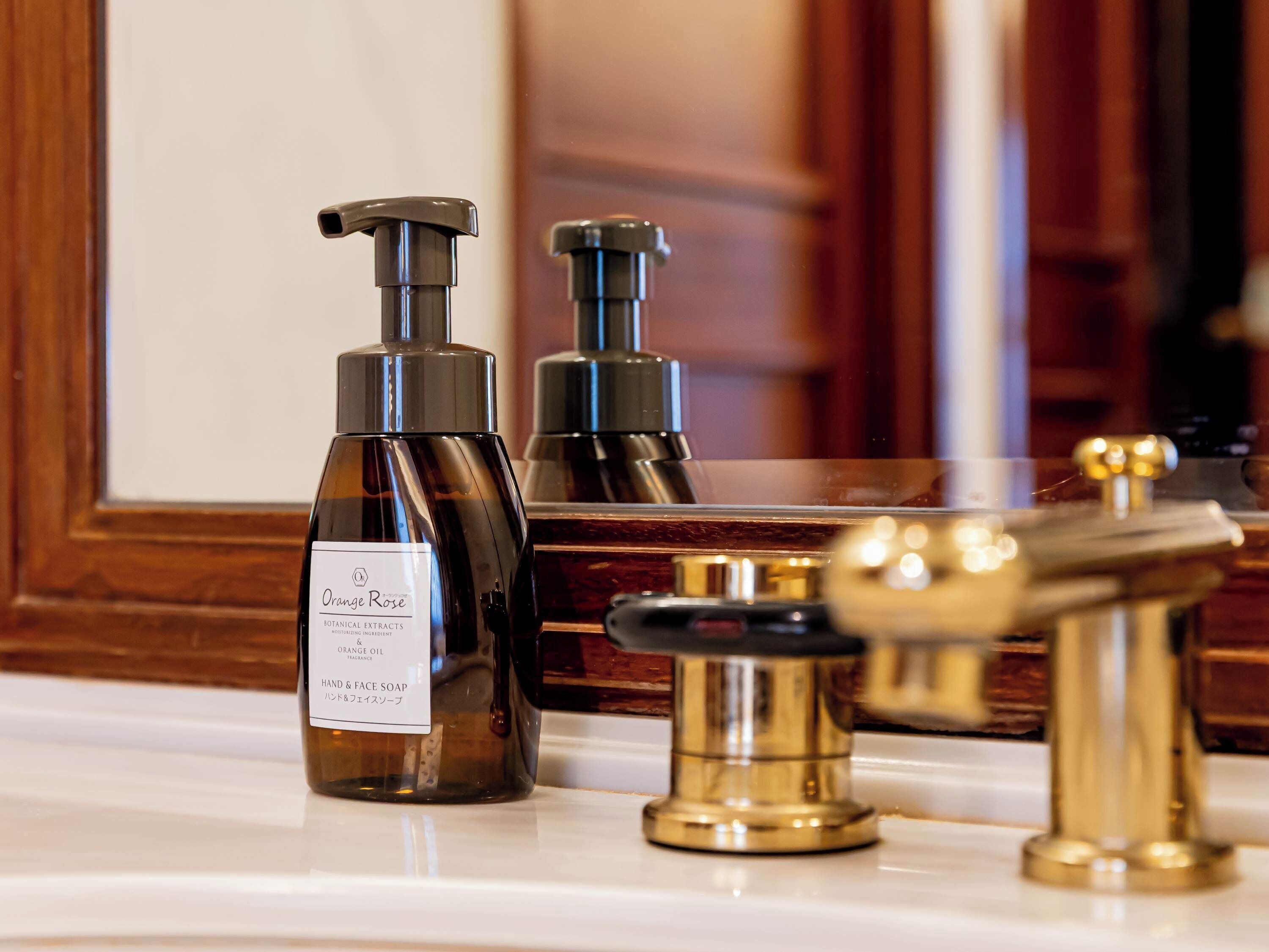 A bathroom vanity with a mirror, a hand and face soap dispenser, and a gold faucet.