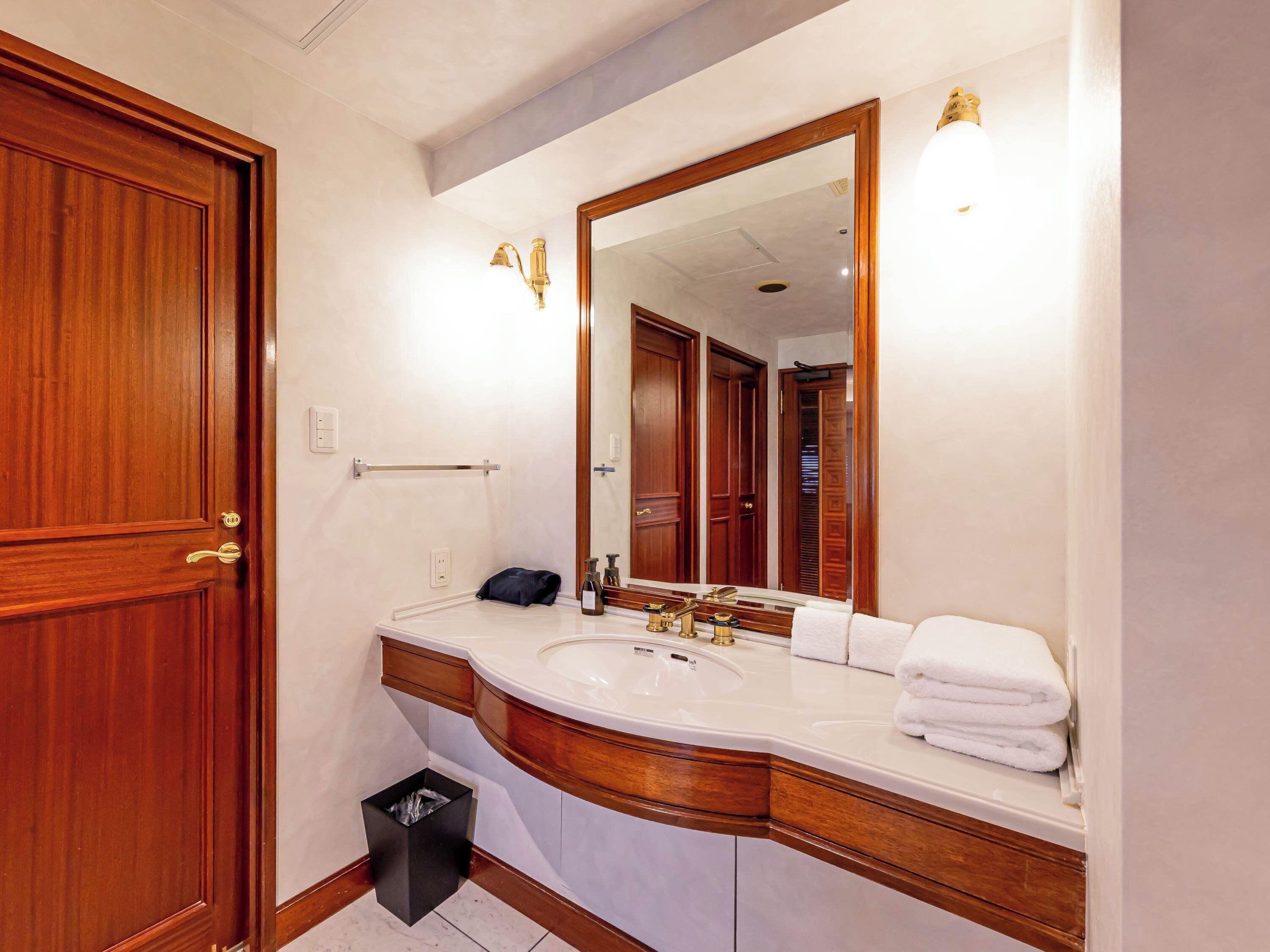 A bathroom with a wooden door, a large mirror, a sink, and a towel rack.