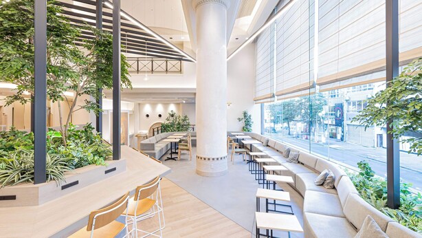 Um espaço interior moderno com uma coluna central, áreas de estar e grandes janelas com vista para a rua.
