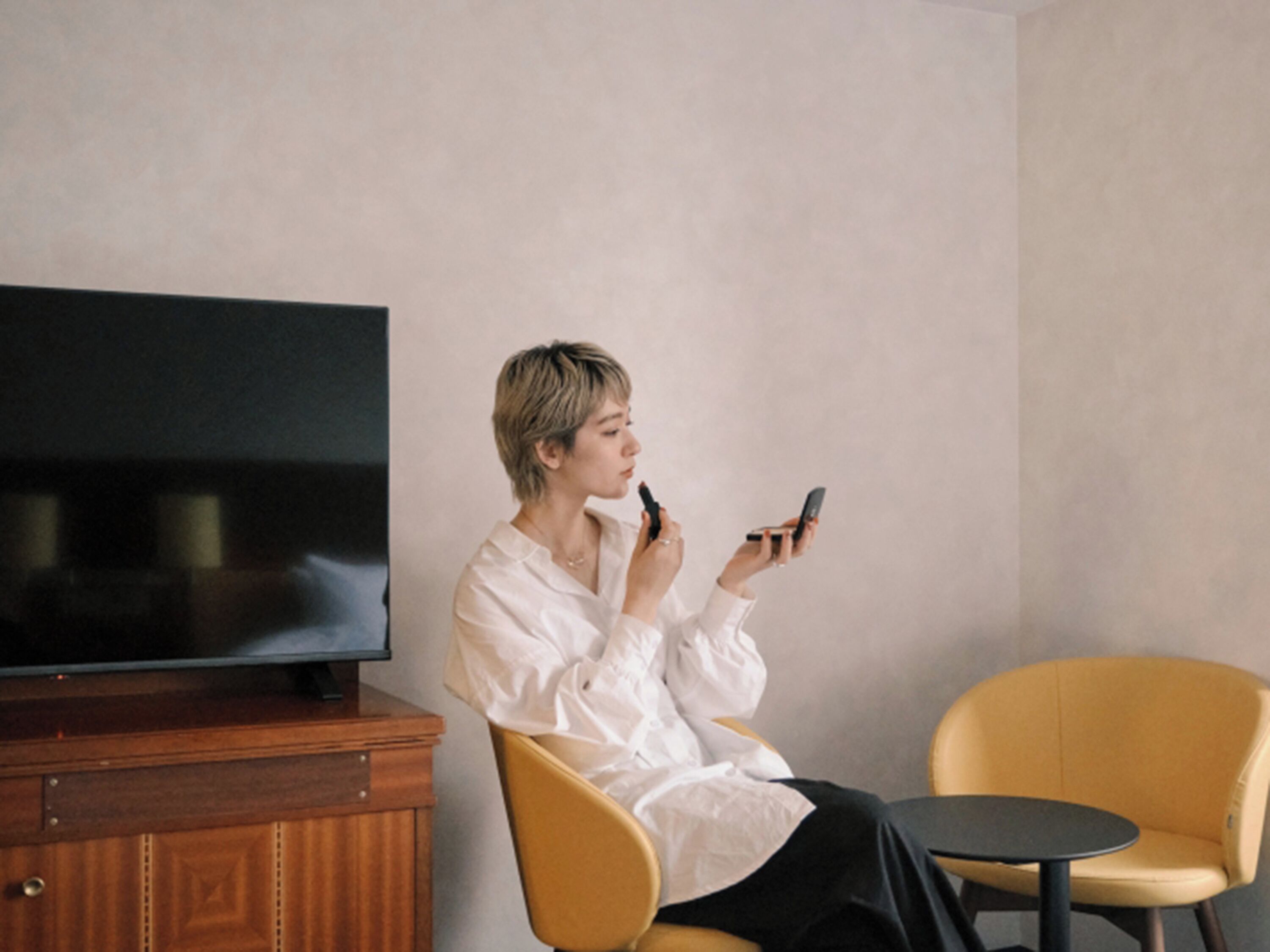 A person sitting on a yellow chair in a room with a wooden cabinet and a flat-screen TV.