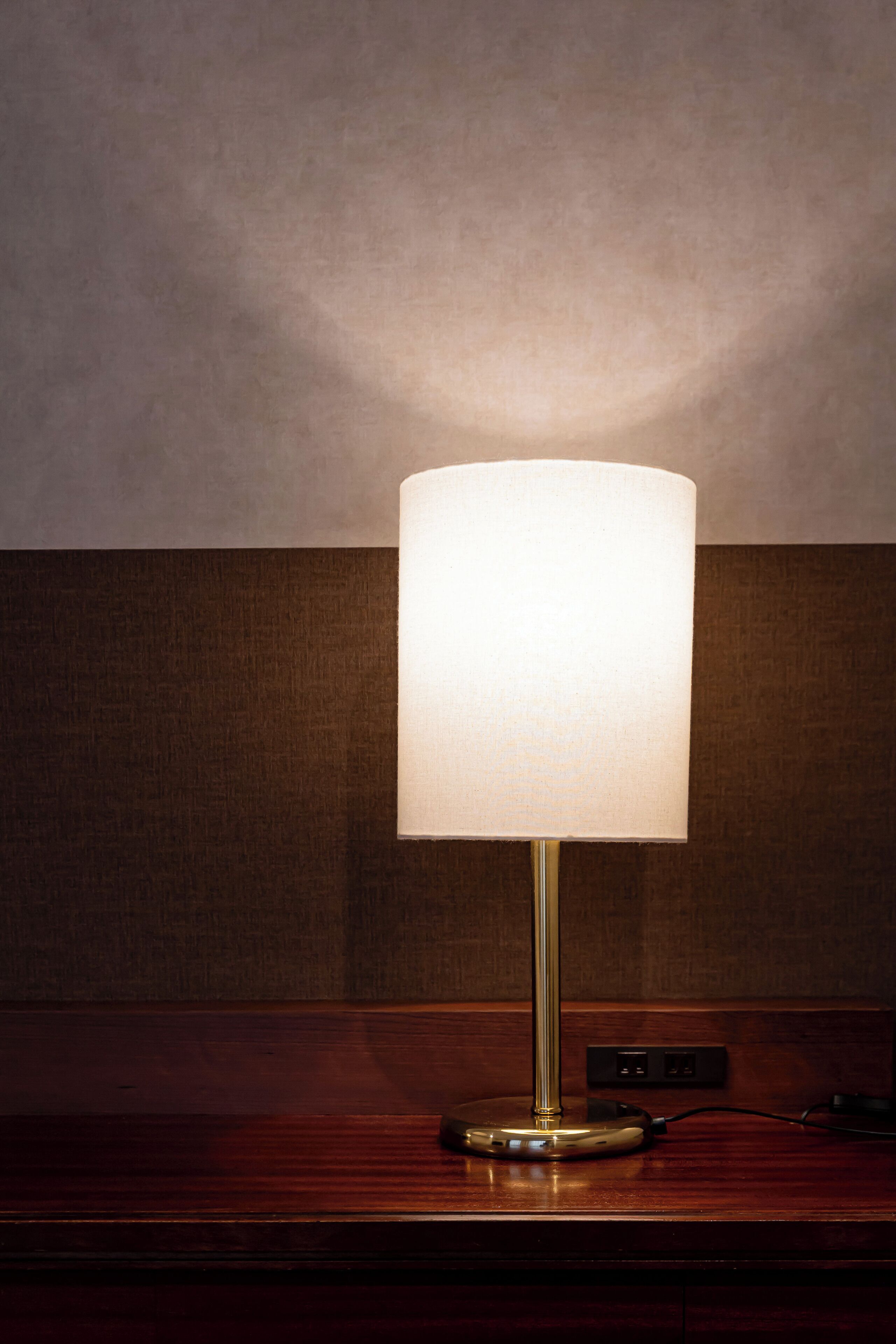 Una lámpara de mesa con pantalla blanca sobre una superficie de madera.
