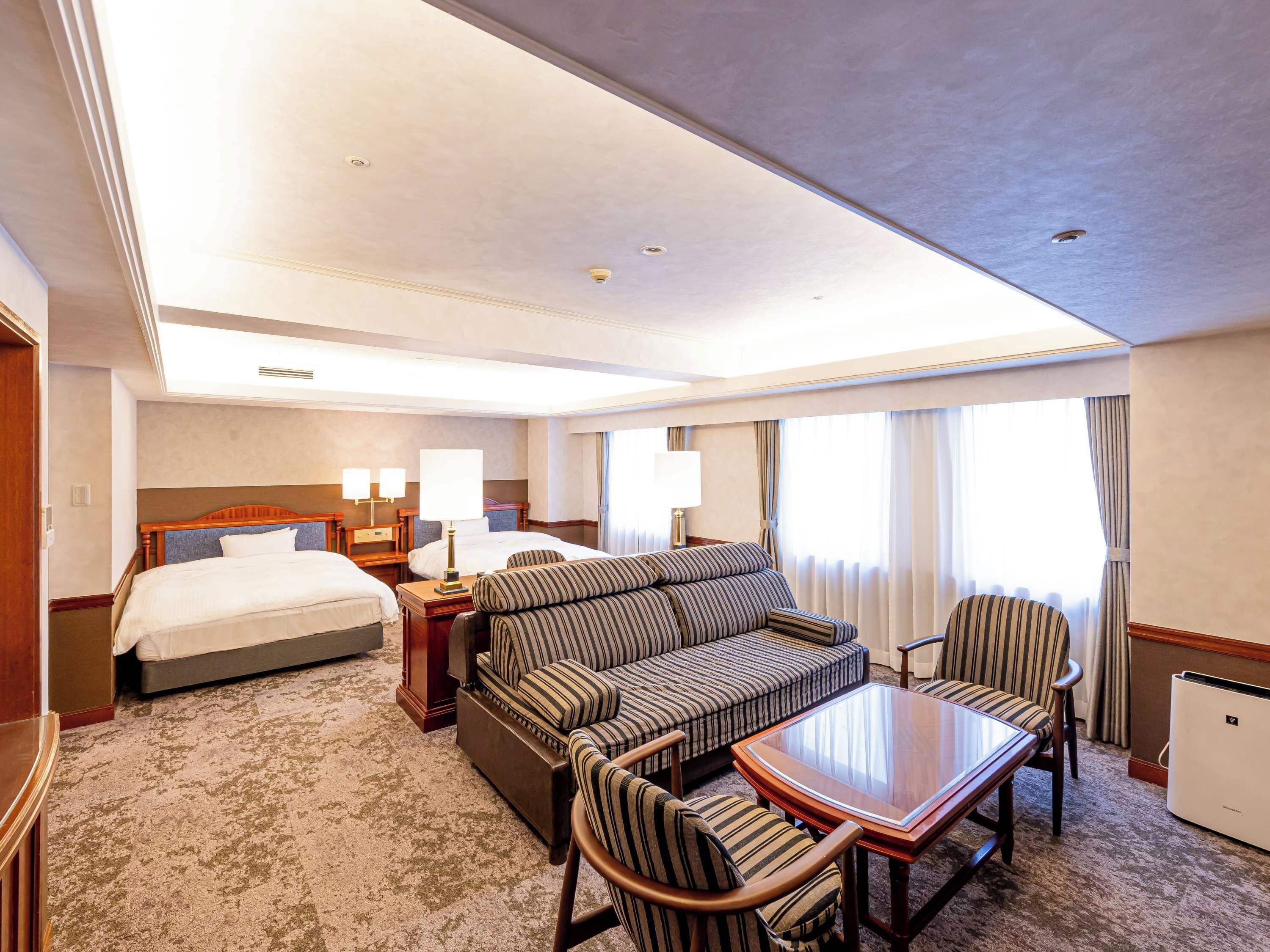 Habitación de hotel con una cama grande, un sofá, una mesa de comedor y una mesita de noche con lámparas.