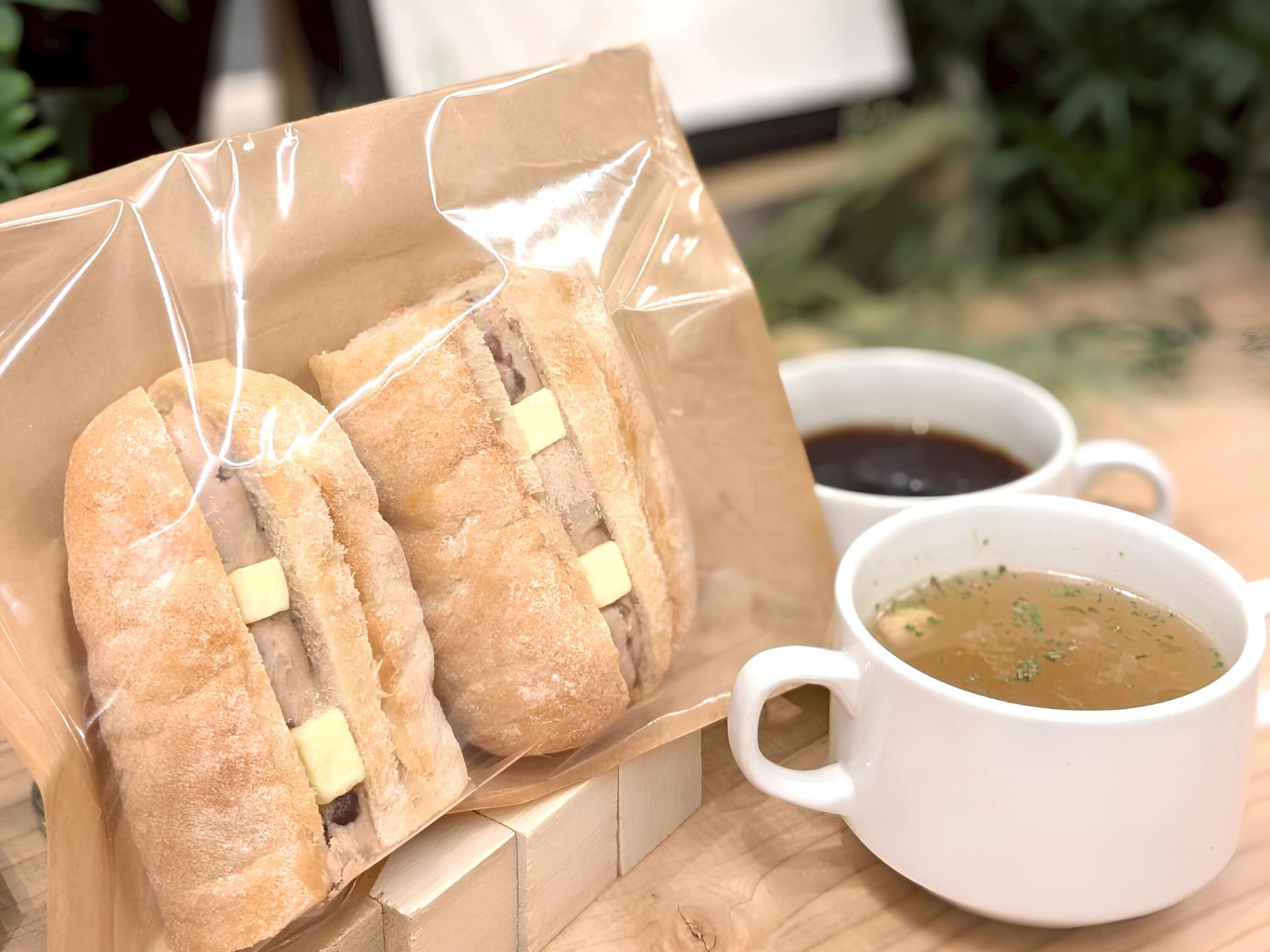 A sandwich in a paper bag with two cups of soup.