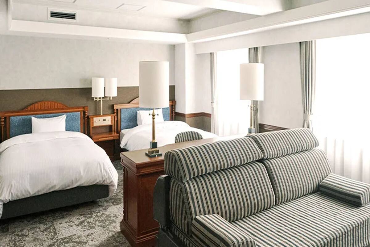 A hotel room with two beds, a sofa, and a desk with lamps.