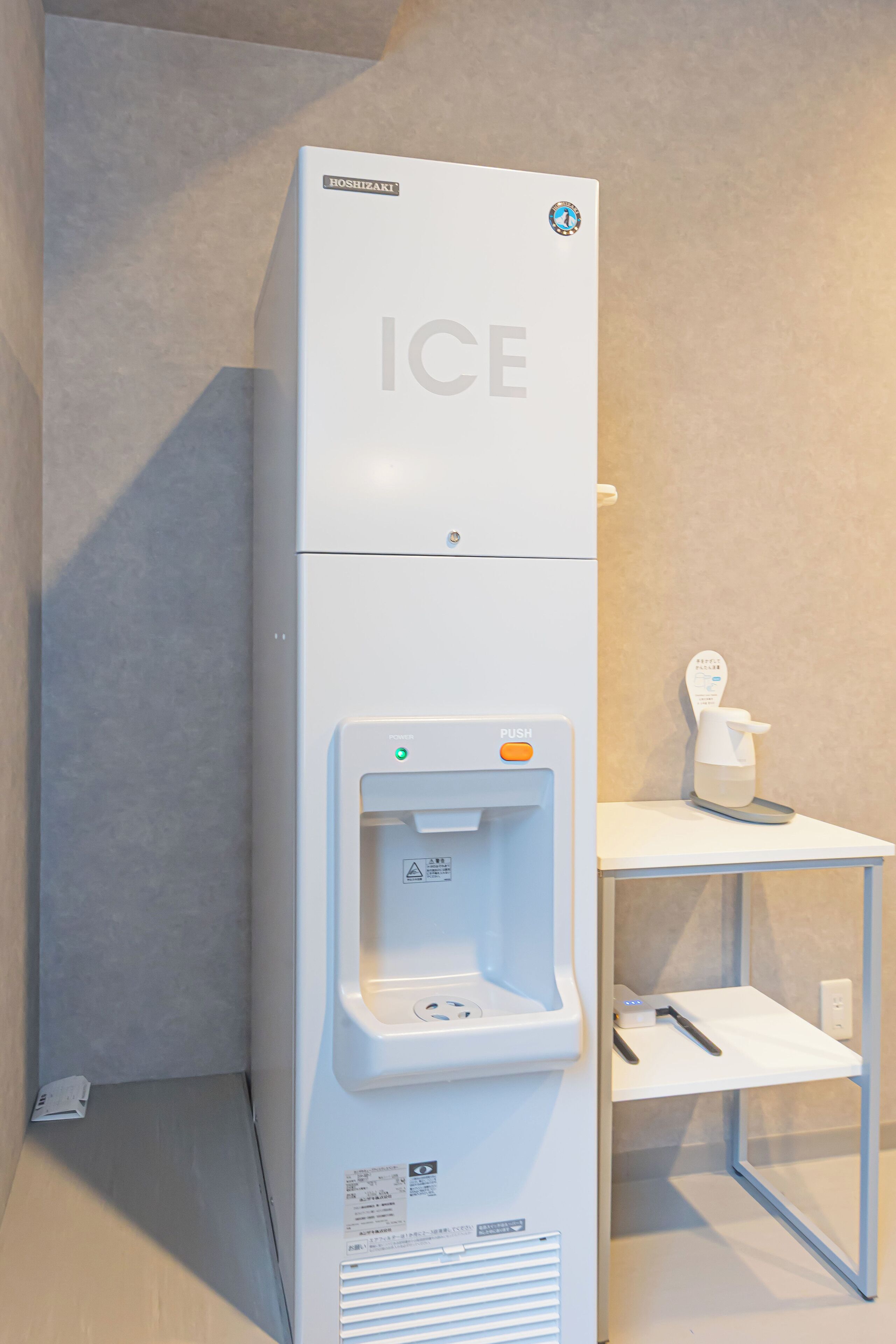 Un distributeur de glaçons blanc, avec le mot « GLACE » inscrit sur le devant, un bouton d’alimentation et un bouton-poussoir.