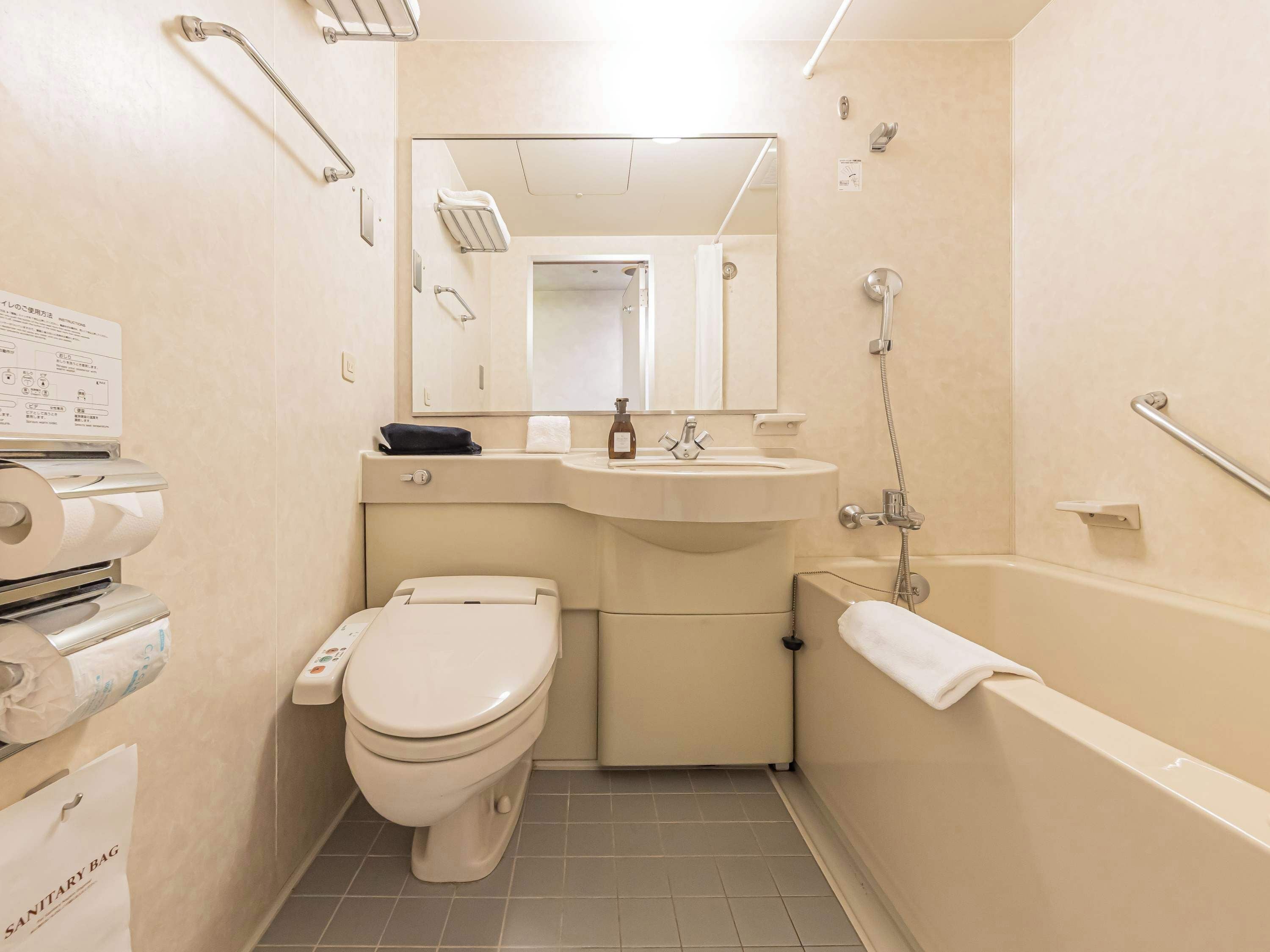 A bathroom with a toilet, sink, and bathtub. There are handrails and a mirror above the sink.