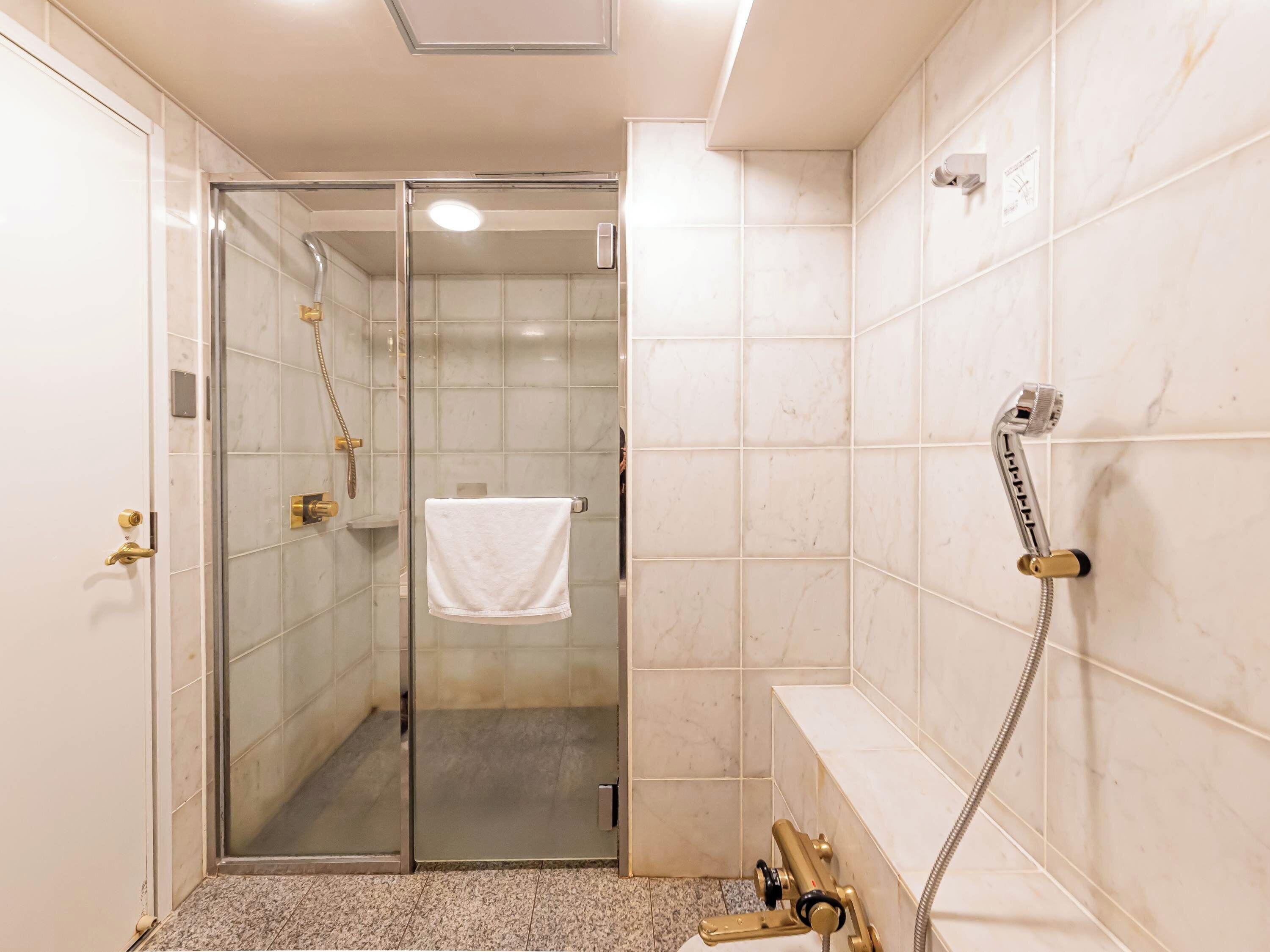 A modern bathroom with a glass-enclosed shower, a white towel hanging on the wall, and a bathtub with a handheld showerhead.