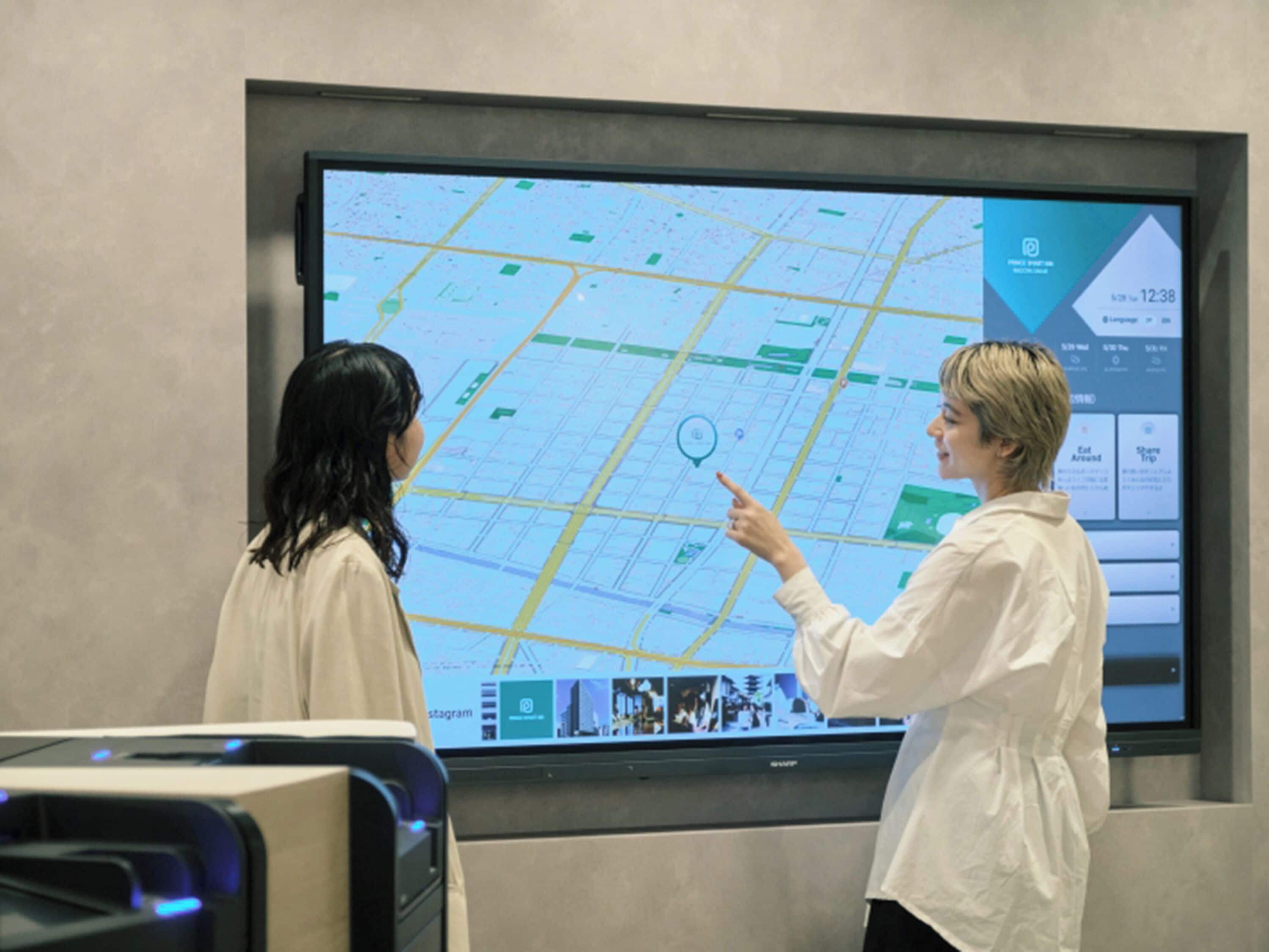 Two people examining a large digital map on a wall.