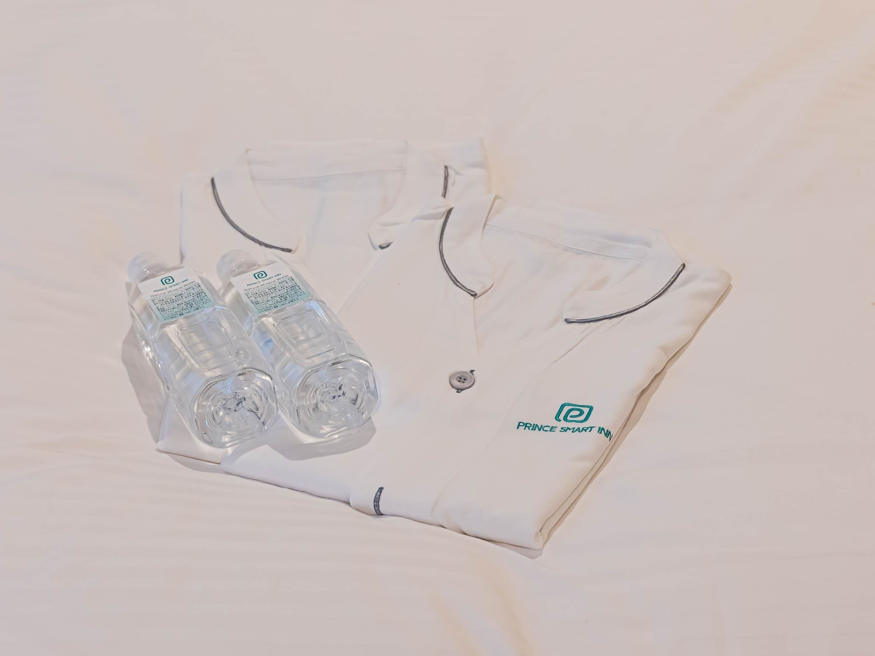 A neatly folded white polo shirt with a logo and two clear plastic water bottles with labels.