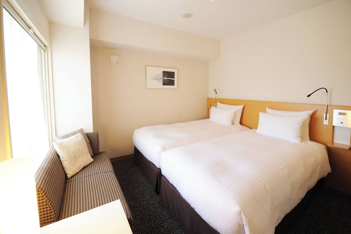 A hotel room with two beds, a sofa, a small table, and a window.