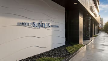 Exterior del Hotel Sunflex Kagoshima, con una fachada moderna, cielo despejado y un camino que lleva a la entrada.