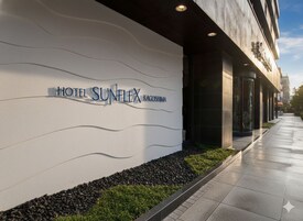 Exterior do Hotel Sunflex Kagoshima com fachada moderna, céu claro e um caminho que leva à entrada.