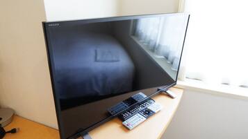Uma televisão de tela plana sobre uma mesa de madeira, com controle remoto e decodificador.