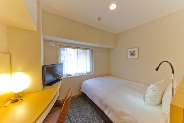 A hotel room with a single bed, a desk with a television, a chair, and a window with curtains.