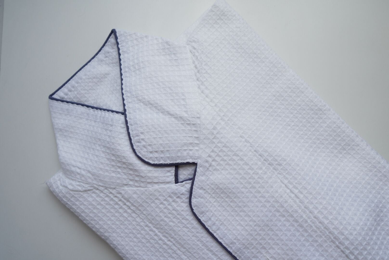A white textured fabric with a dark trim, likely a piece of clothing or upholstery.
