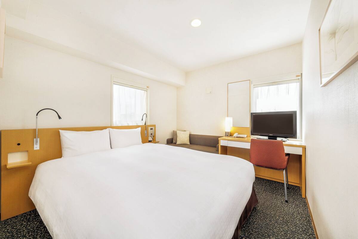 A hotel room with a large bed, a desk with a chair, a television, and a window.