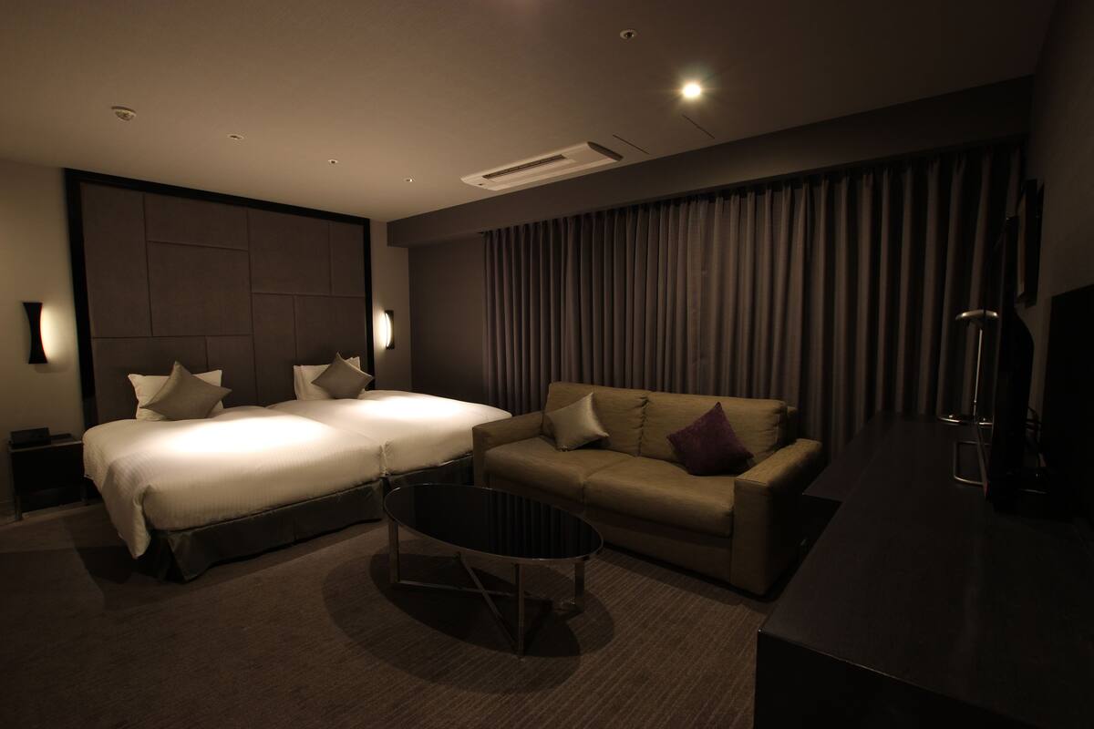 A hotel room with a large bed, a sofa, a small table, and a TV.