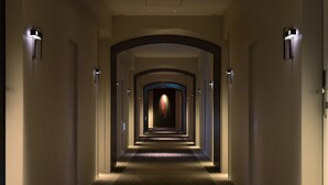Un largo y estrecho pasillo de hotel con varias puertas y lámparas en las paredes.