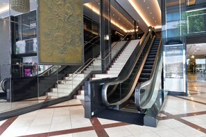 Un interior moderno con una escalera mecánica central, barandillas de vidrio y un revestimiento de pared estampado.