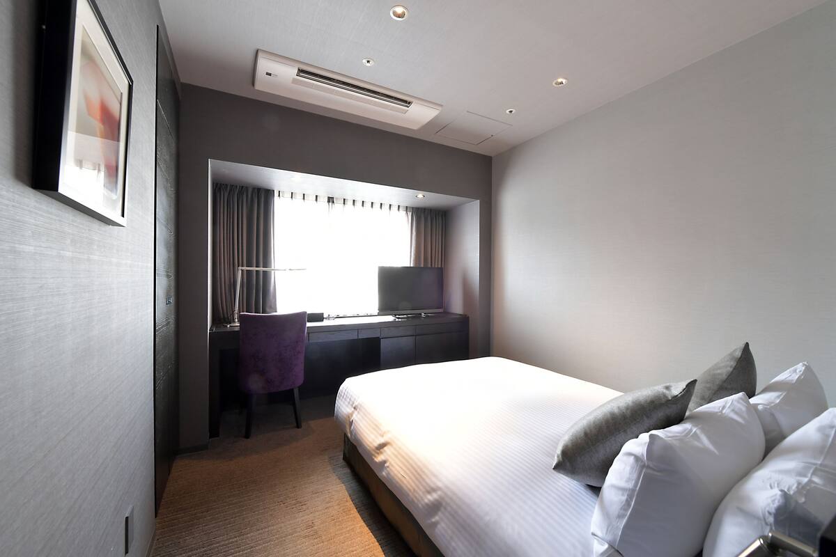 A modern hotel room with a large bed, a desk with a chair, and a television.