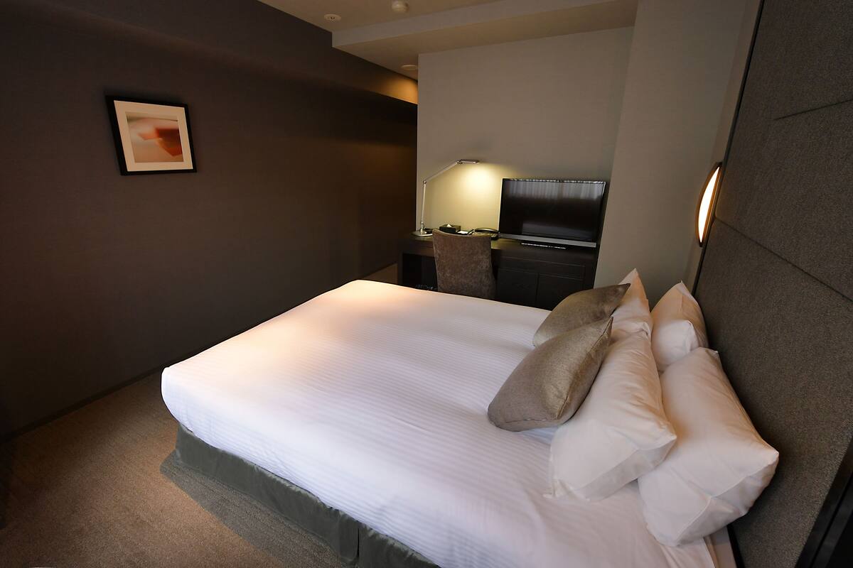 A neatly made bed with white linens and several pillows, a bedside table with a lamp, and a framed picture on the wall.