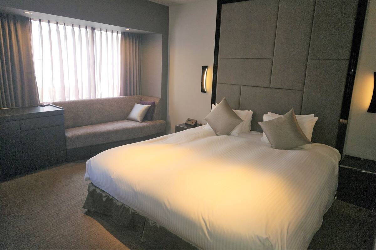 A hotel room with a large bed, a sofa, a nightstand, and a wall-mounted lamp.
