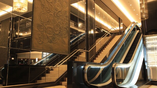 Un interior moderno con escaleras mecánicas y una escalera, una araña y una pared decorativa.