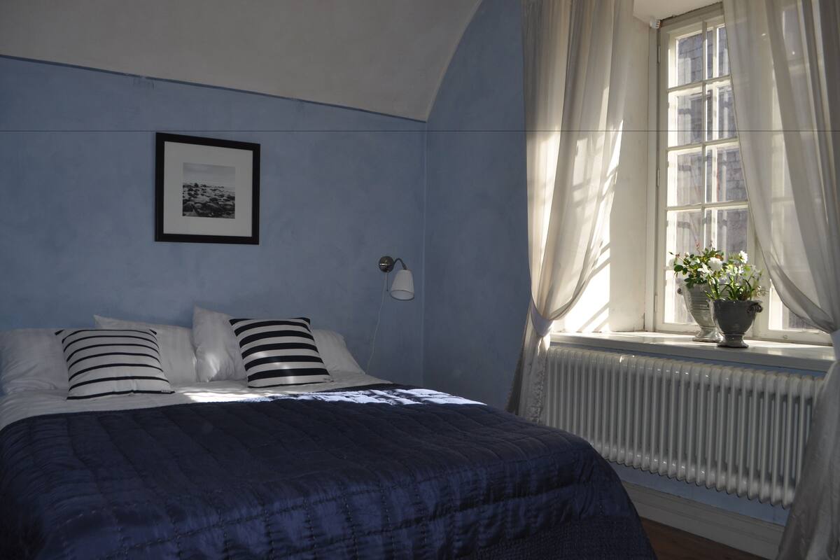 Ein Schlafzimmer mit einem Bett, einem gerahmten Bild an der Wand, einem Fenster mit Vorhängen und einer Heizung.