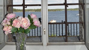 Una ventana con vistas al agua y un barco. En el alféizar, un florero con flores y una figurita de rana.