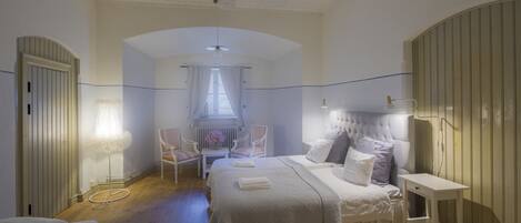 A bedroom with a large bed, a chair, a bedside table, and a window with curtains.