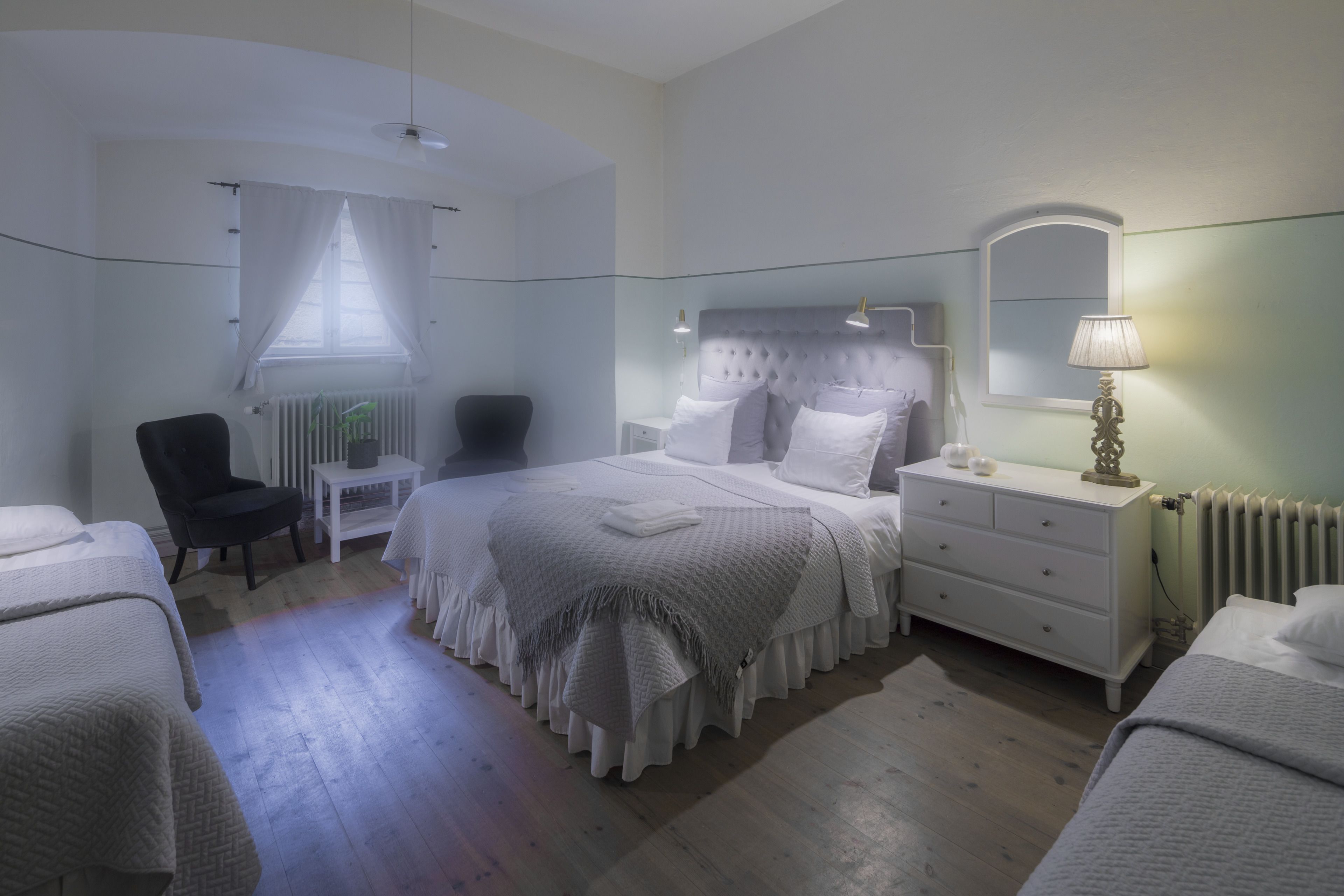A bedroom with a bed, a chair, a dresser, and a lamp.