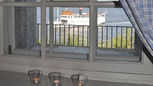 Una ventana con vista a un bote en el agua, una barandilla y tres velas encendidas en un estante debajo.