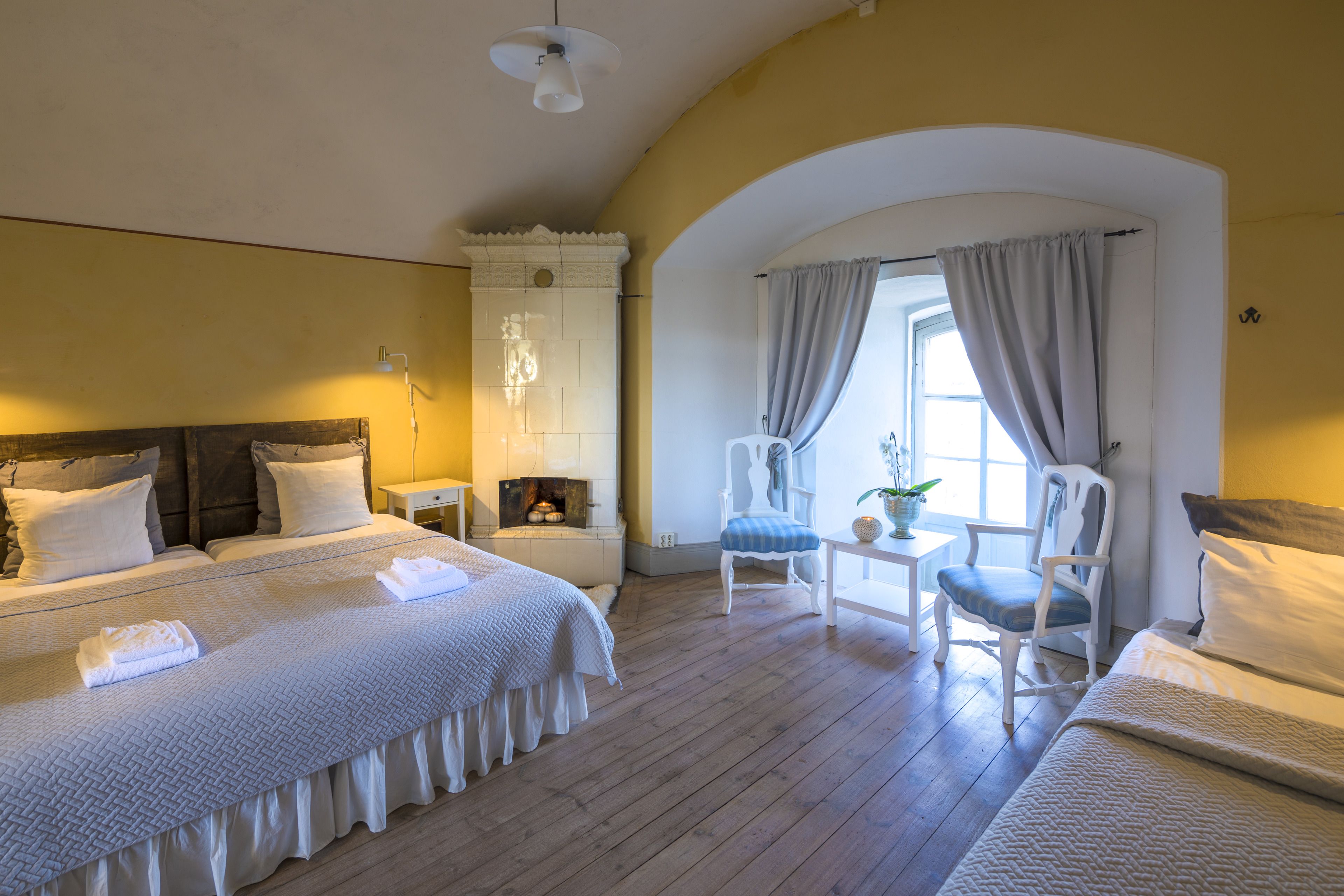 A hotel room with a large bed, two chairs, a small table, and a window with curtains.