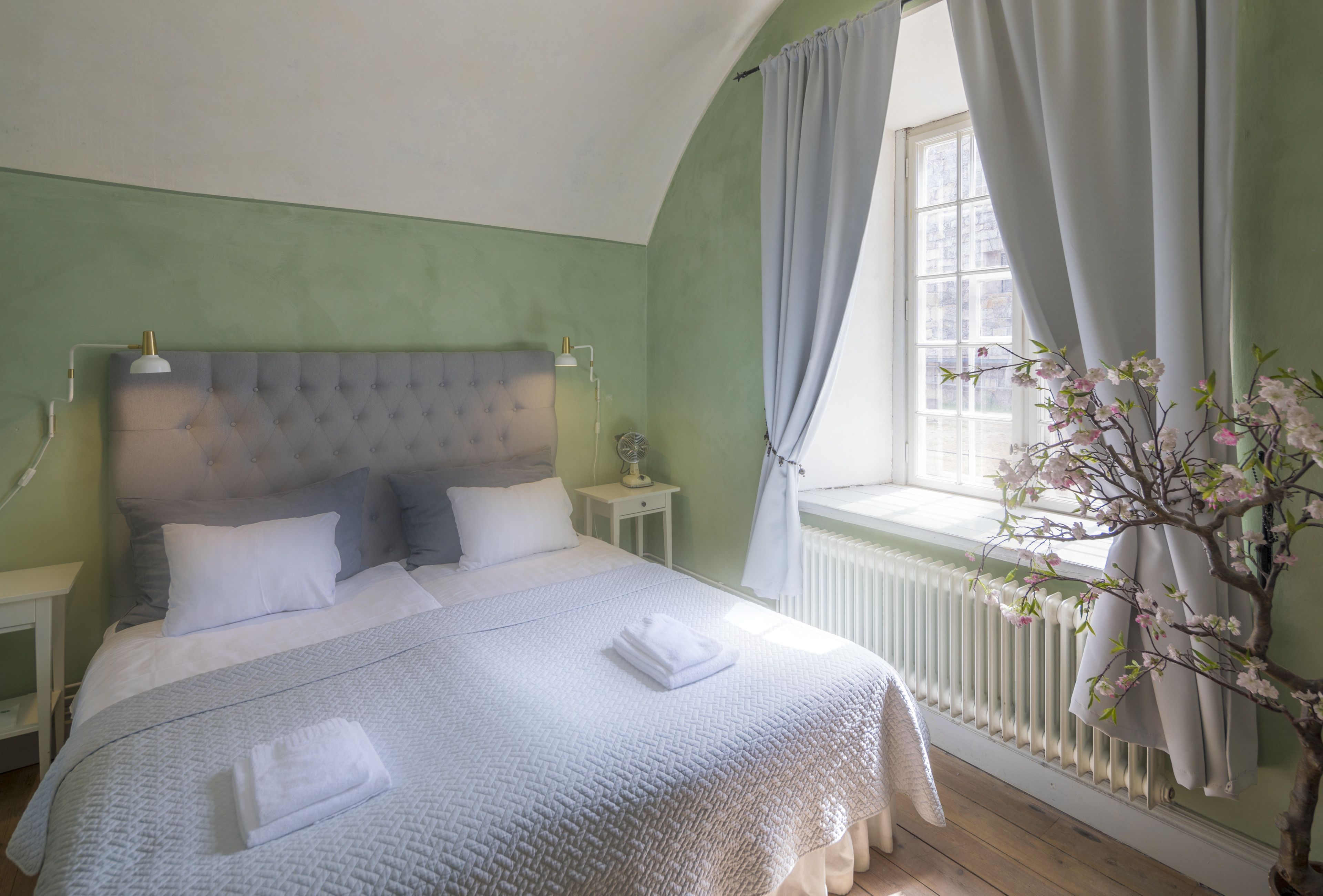 Un lit bien fait, avec du linge de lit blanc, une tête de lit capitonnée et une table de chevet avec une lampe.