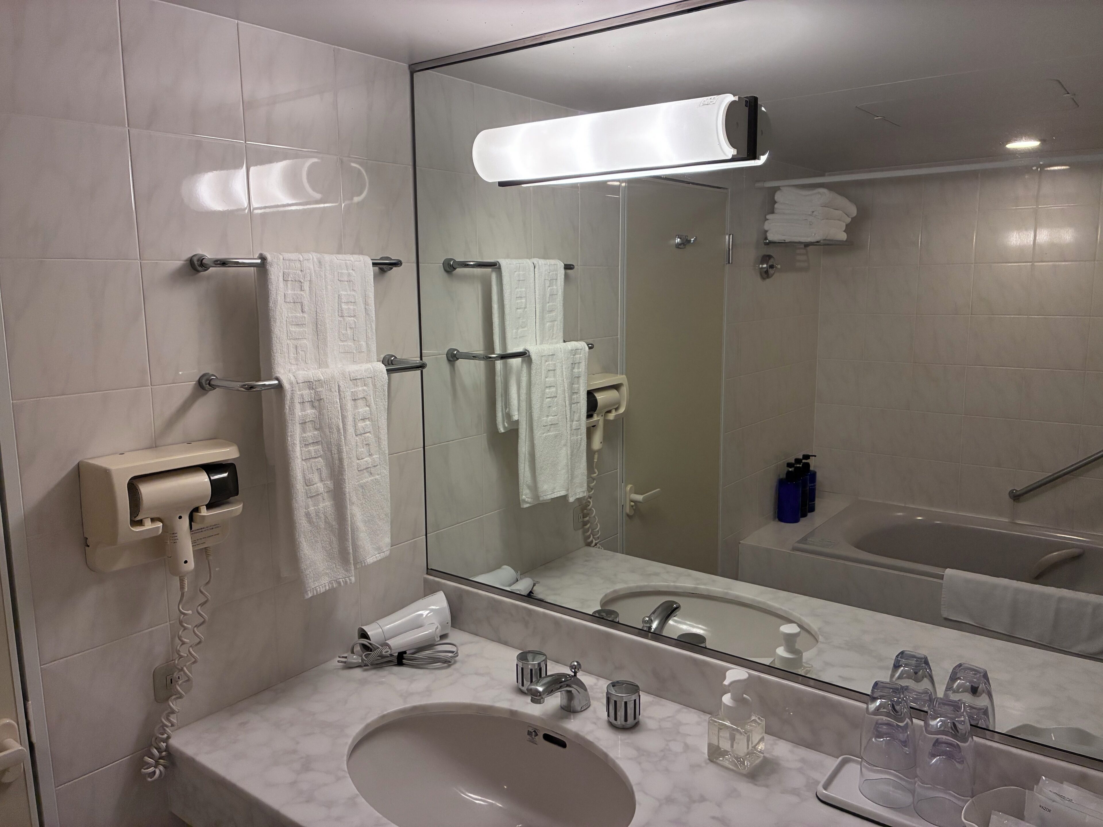 A bathroom with a sink, mirror, towel rack, hair dryer, and toiletries.