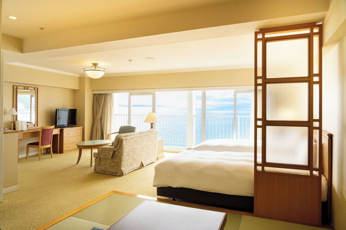 Habitación de hotel con cama, escritorio, silla, televisión y vista al océano.