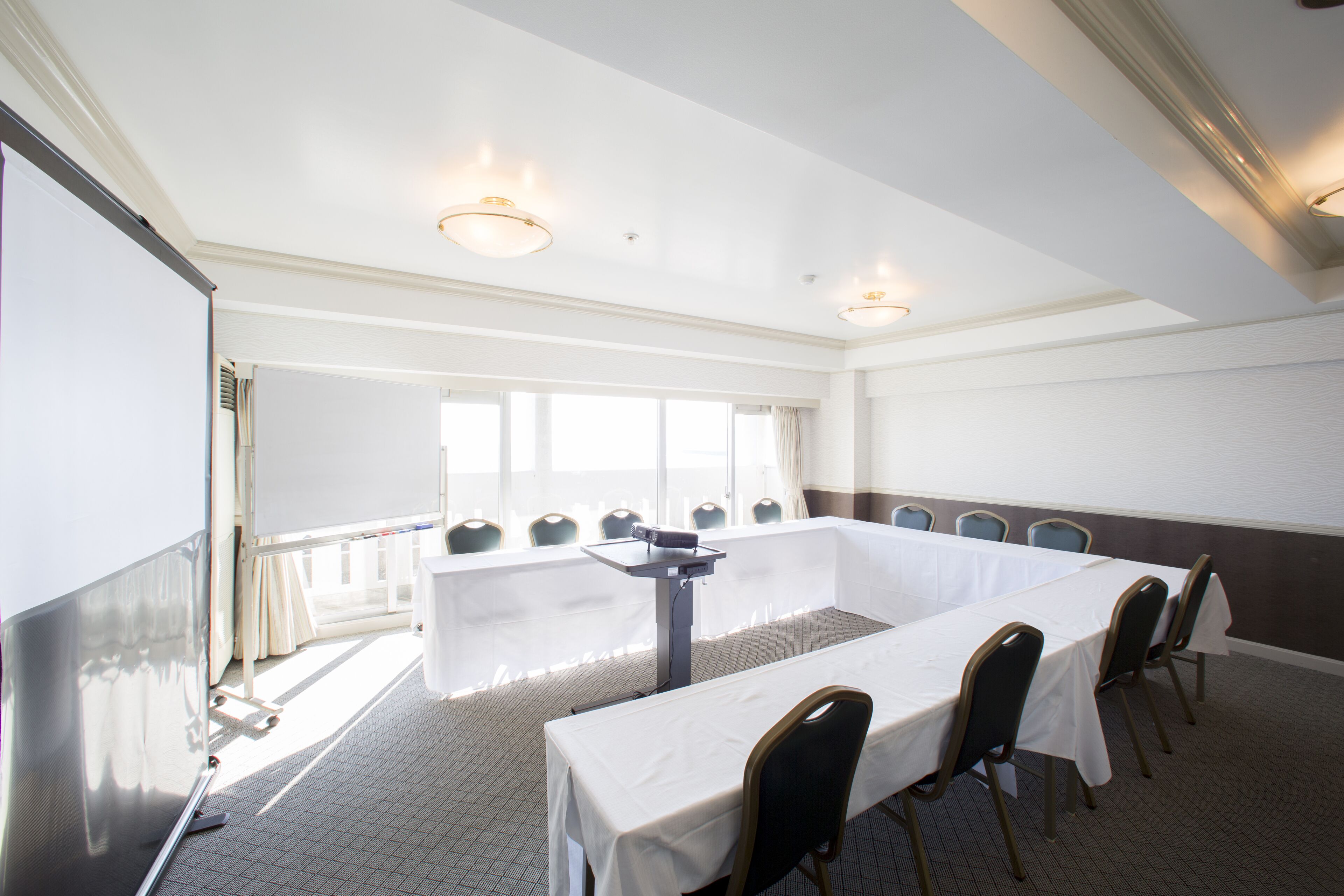 A conference room with a long table, chairs, a projector screen, and a large window.
