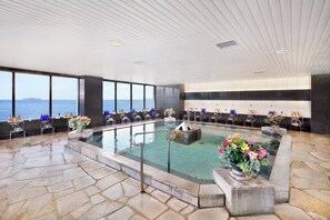 Una amplia piscina cubierta con vistas al mar, suelo de piedra y zona de bar con asientos y servicios.