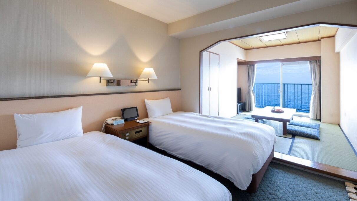 Une chambre d’hôtel avec deux lits, un bureau, une chaise et un balcon donnant sur la mer.