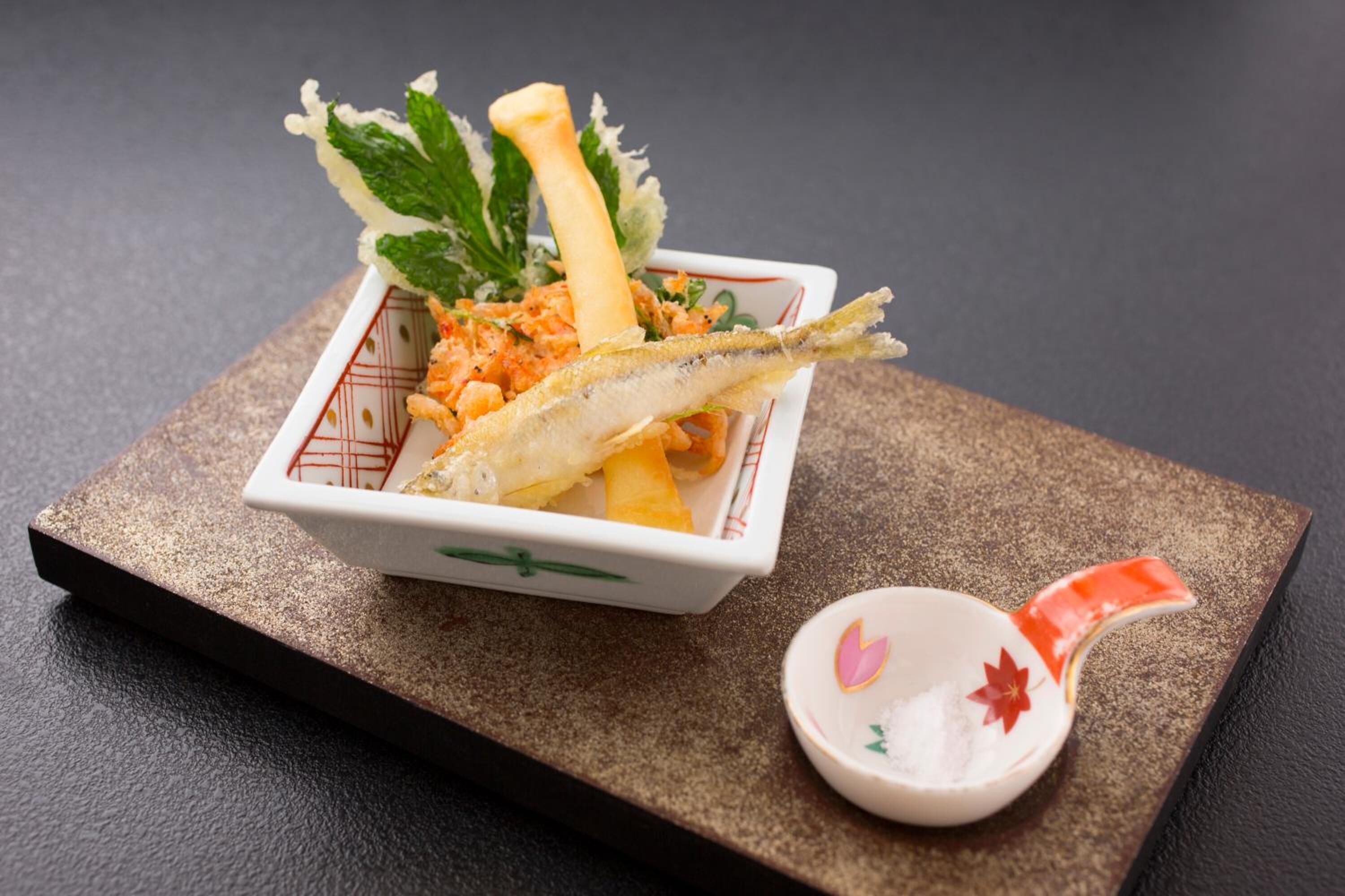 A dish with fish, vegetables, and a decorative leaf on a textured surface.
