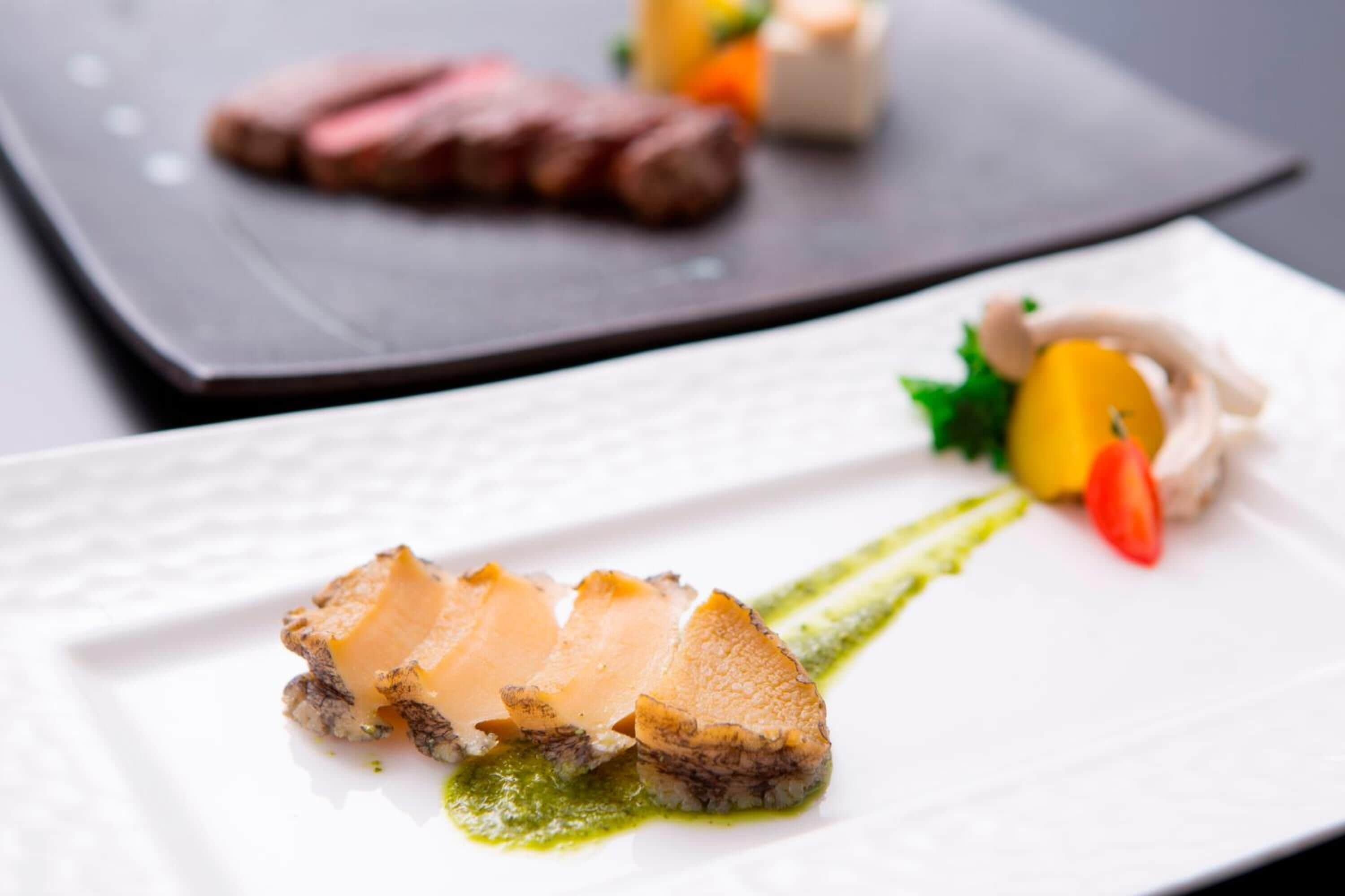 A plate with sliced meat, a small fruit, and a sauce.