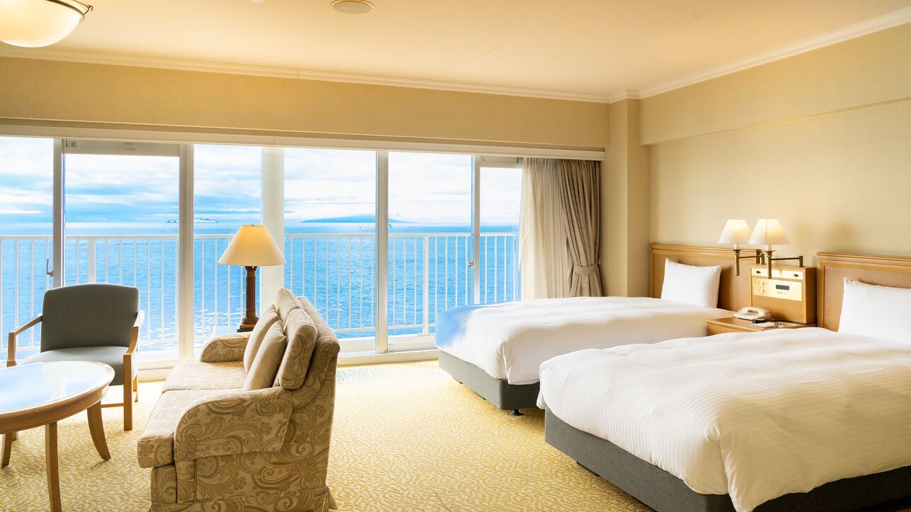 Une chambre d’hôtel avec deux lits, un canapé, une table, une lampe et une vue sur la mer.