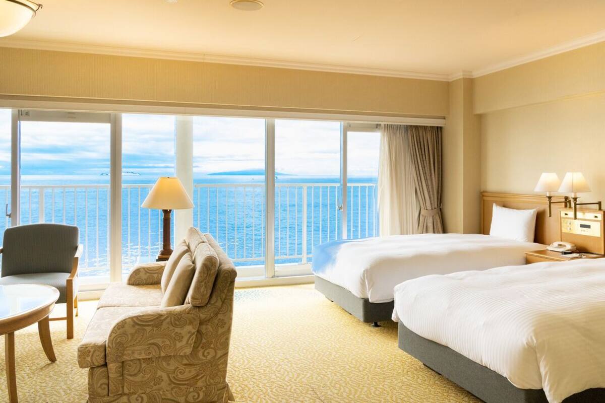 Habitación de hotel con dos camas, un sofá, una mesa, una lámpara y vista al mar.