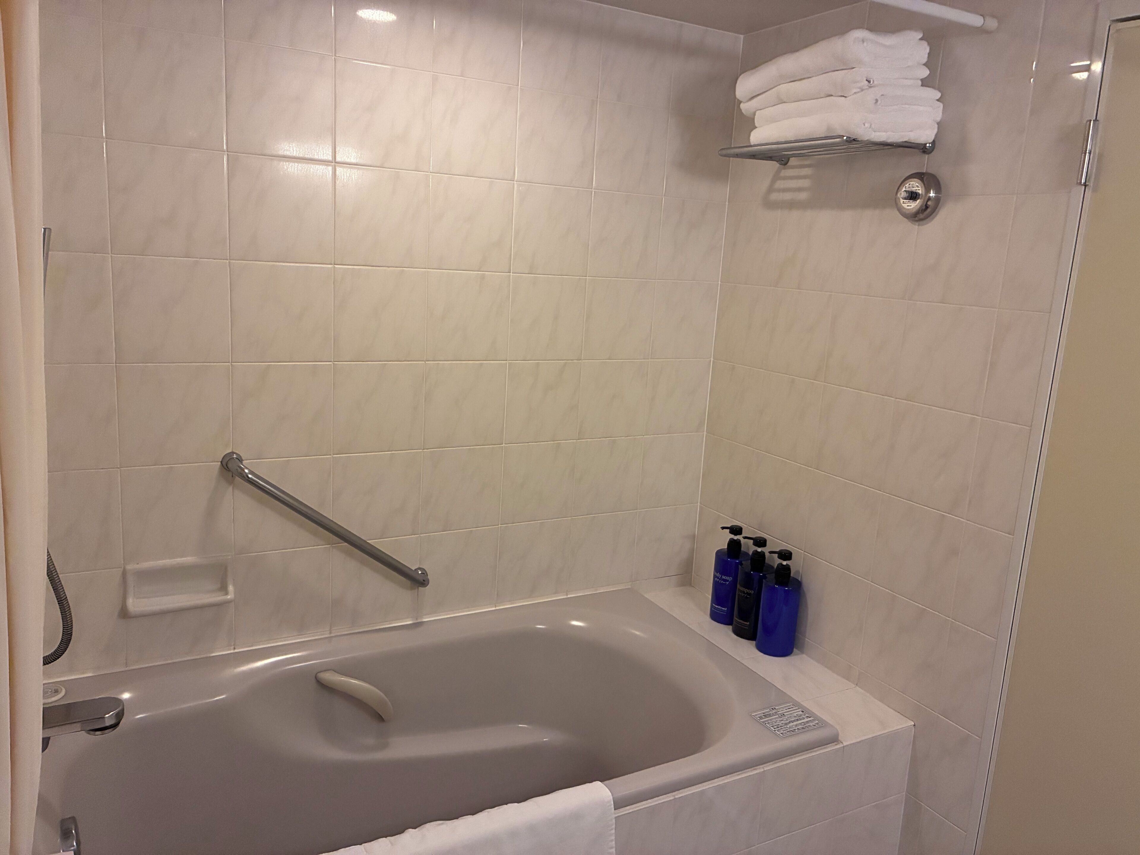 Un baño moderno con bañera, barandilla, estante con artículos de aseo y toallero.