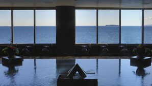 A room with a large window overlooking the sea, featuring a central pillar and seating area with potted plants. - Resorpia Atami (Atami)